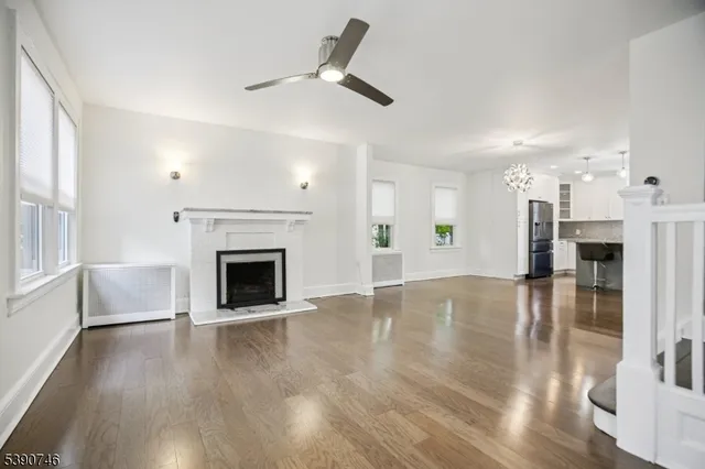 a view of a livingroom with a fireplace a ceiling fan and windows