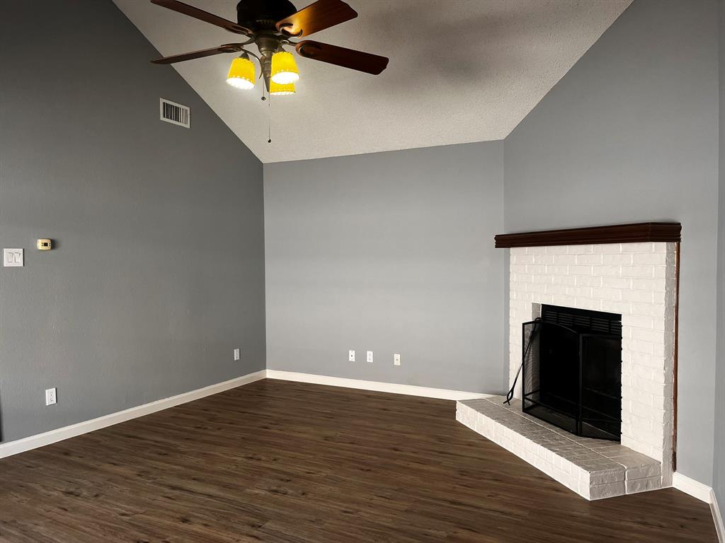 1007 Mack Place Denton, TX 76209 - Photo 13 of 37 Unfurnished living room with dark wood-style flooring, a ceiling fan, vaulted ceiling, and a brick fireplace