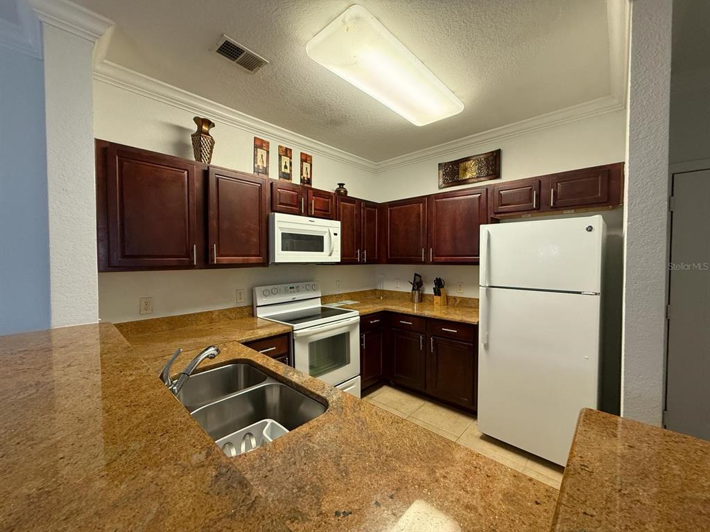 1361 Tuscan Terrace, Unit 7307 Davenport, FL 33896 - Photo 7 of 22 a kitchen with stainless steel appliances granite countertop a refrigerator a stove and a sink with wooden floor