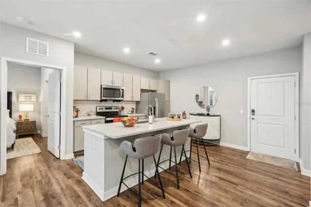 a kitchen with stainless steel appliances a stove top oven a refrigerator a sink and a dining table with wooden floor