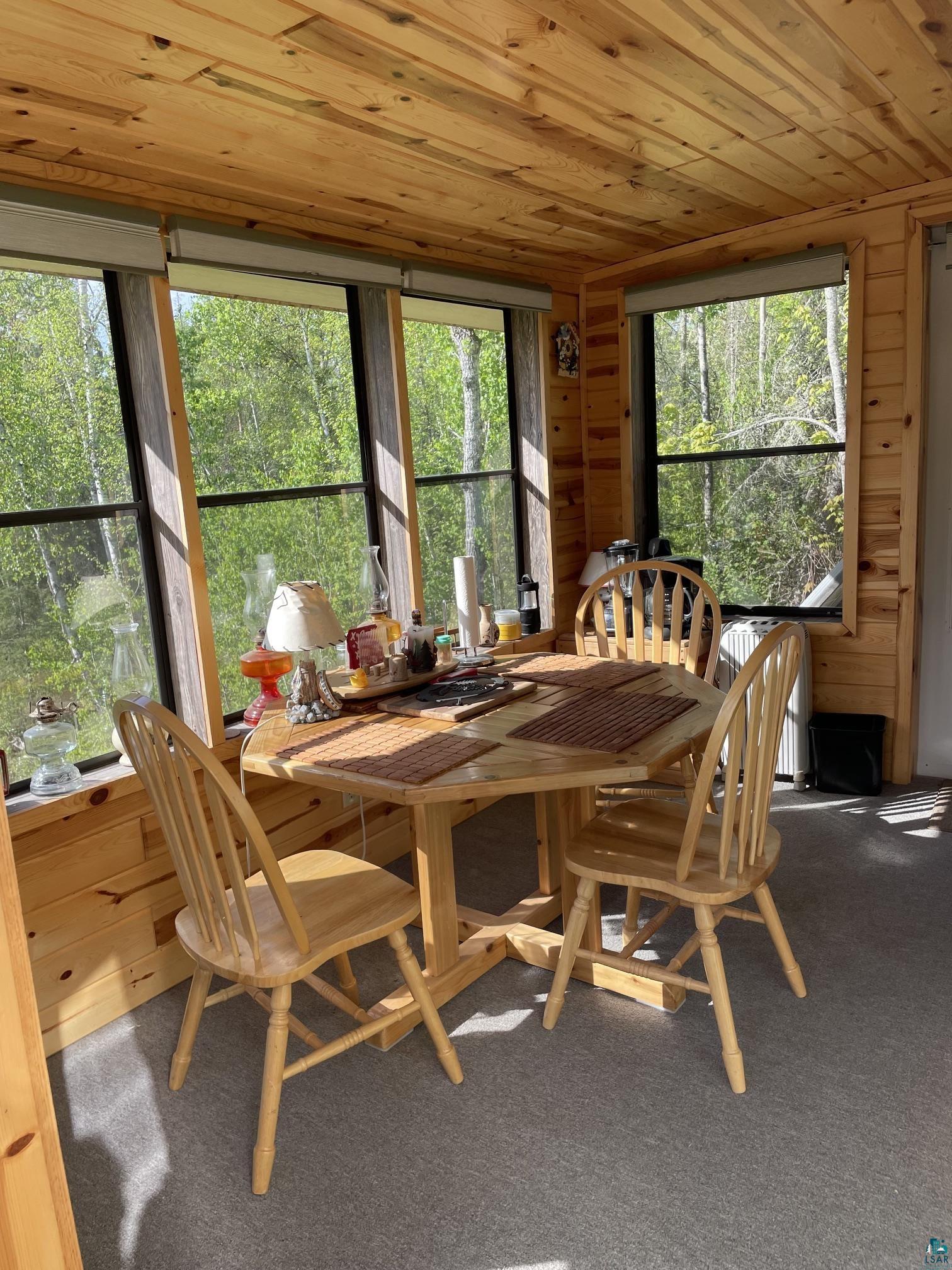 1152 Fernberg Road Ely, MN 55731 - Photo 7 of 24 Sunroom featuring wood-paneled walls and ceiling, multiple windows, gray carpet flooring, and a built-in wall-mounted fixture
