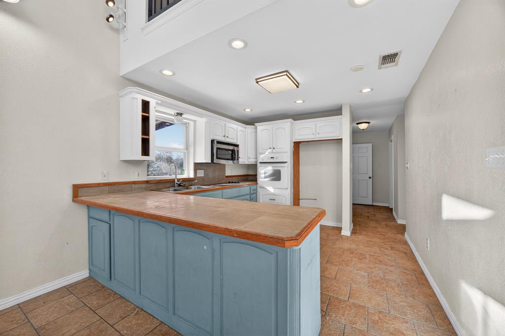 6775 Silver Creek Azle Road Azle, TX 76020 - Photo 11 of 40 Kitchen featuring a peninsula, stone tile floors, white cabinetry, white oven, and stainless steel microwave