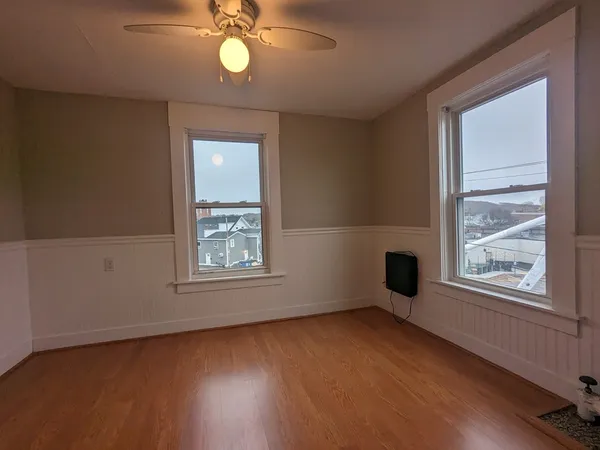 an empty room with wooden floor fan and windows