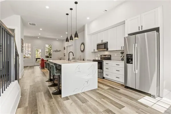 a kitchen with stainless steel appliances kitchen island granite countertop a refrigerator a stove oven and white cabinets with wooden floors