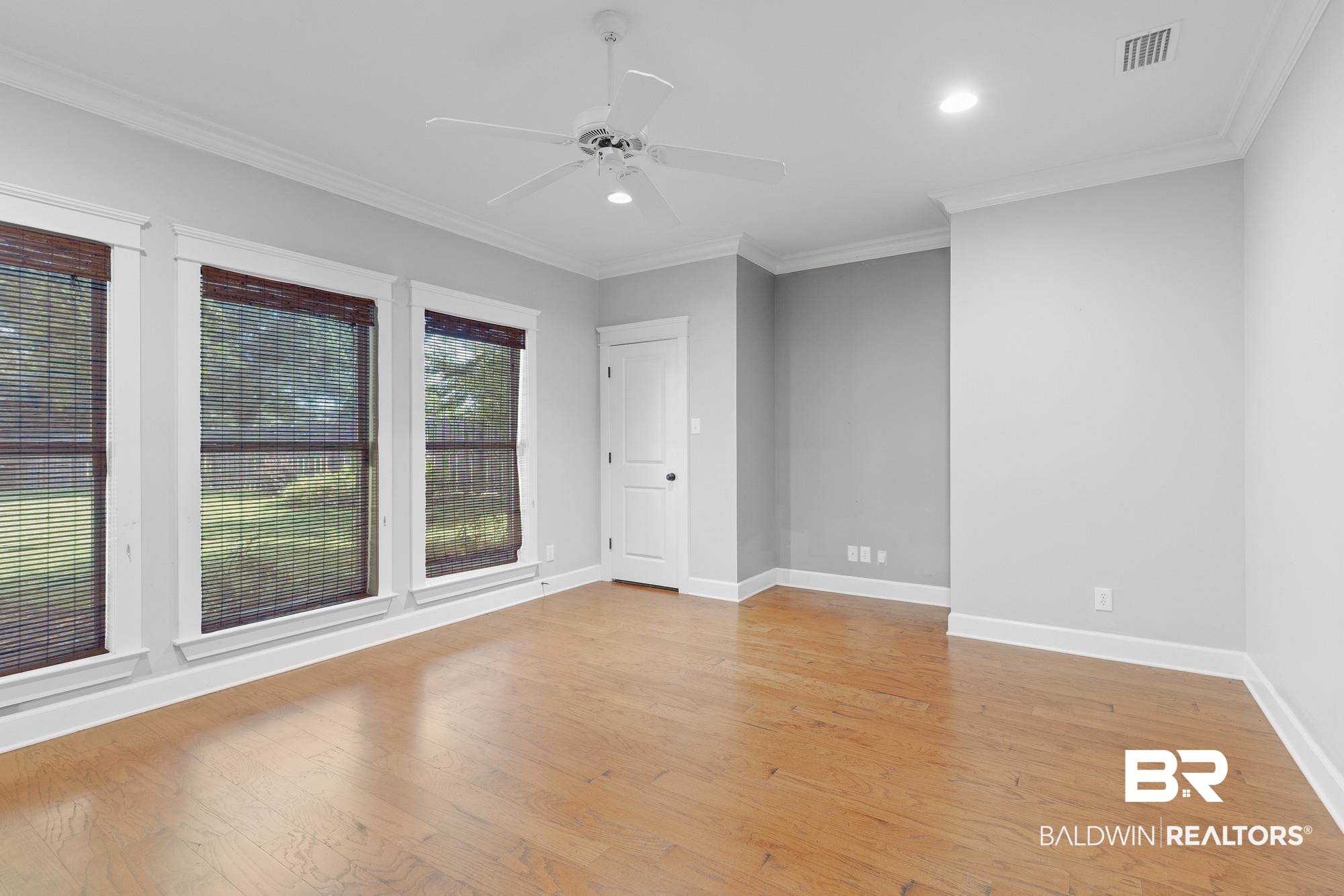 11261 Halcyon Loop Daphne, AL 36526 - Photo 25 of 41 Interior room featuring wood-finish flooring, three windows with woven blinds, and a white ceiling fan with integrated lighting