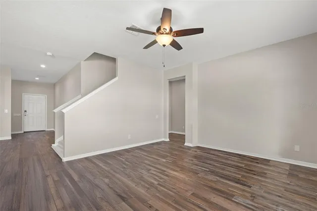 a view of an empty room with wooden floor and a ceiling fan