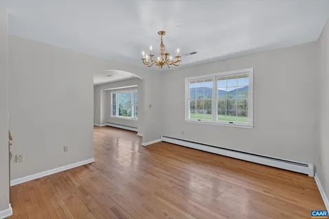 an empty room with wooden floor chandelier and windows