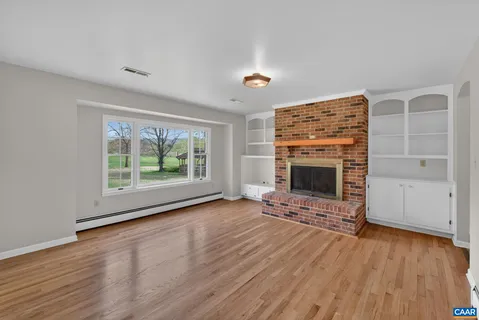 an empty room with wooden floor fireplace and windows