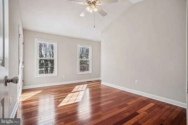 an empty room with wooden floor chandelier fan and windows