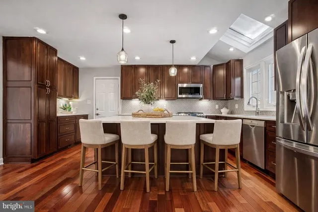 a kitchen with stainless steel appliances granite countertop a dining table chairs refrigerator and microwave