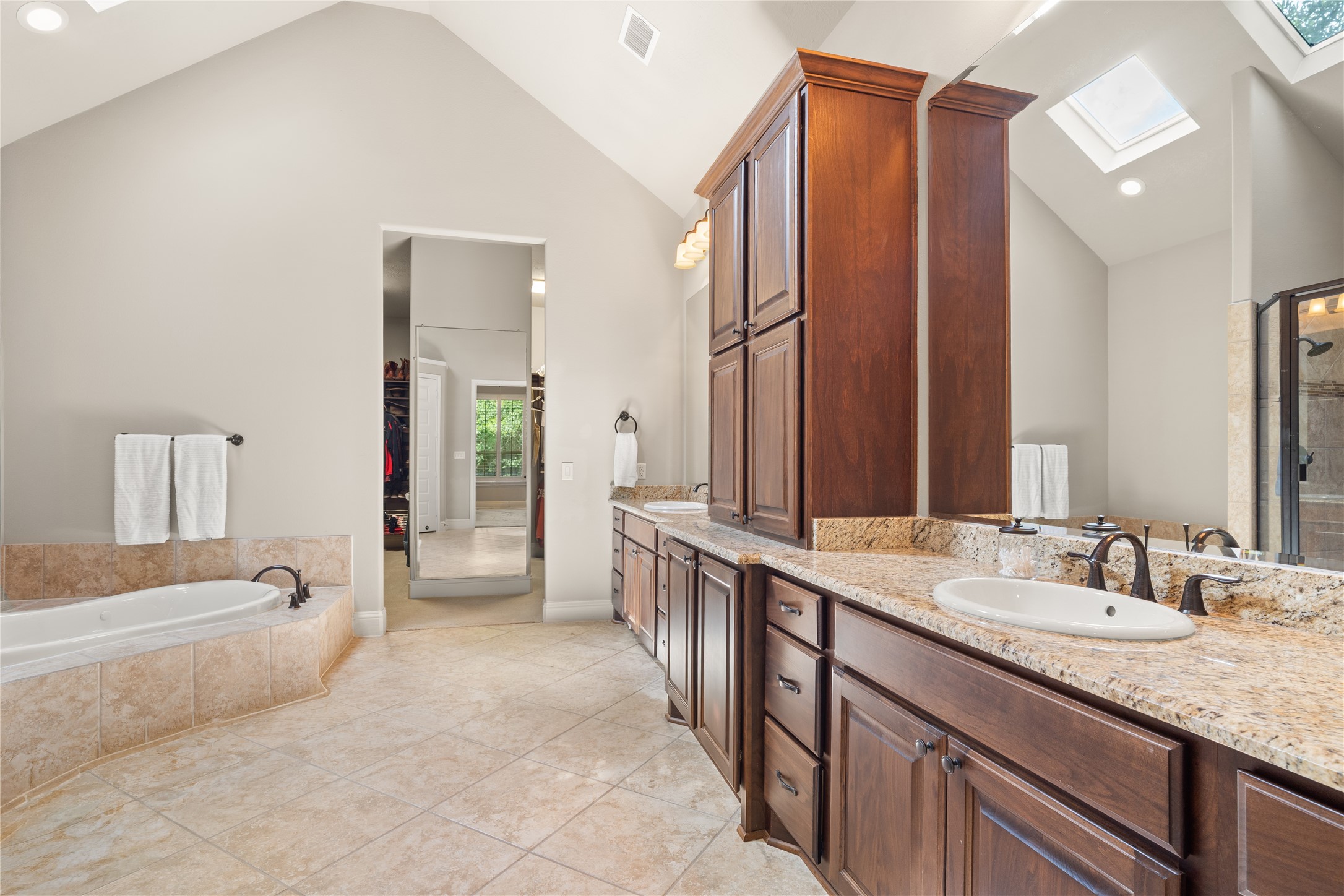 19813 Cullen Ridge Drive Porter, TX 77365 - Photo 23 of 44 This luxurious primary bathroom boasts high vaulted ceilings, elegant granite countertops, rich wooden cabinetry, and abundant natural light from skylights, creating a serene and sophisticated spa-like retreat.
