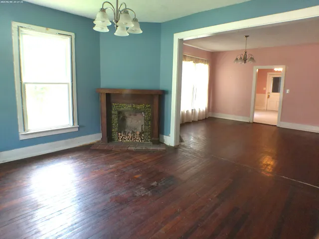 an empty room with wooden floor fireplace and windows