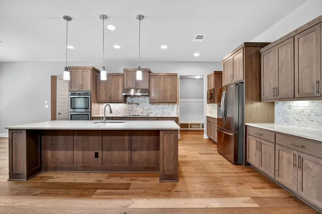 a large kitchen with stainless steel appliances kitchen island granite countertop a refrigerator and a sink