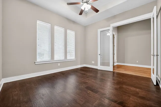 an empty room with wooden floor chandelier fan and windows