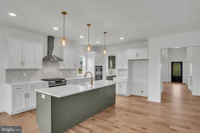 a kitchen with stainless steel appliances granite countertop a sink a stove a refrigerator and white cabinets with wooden floor