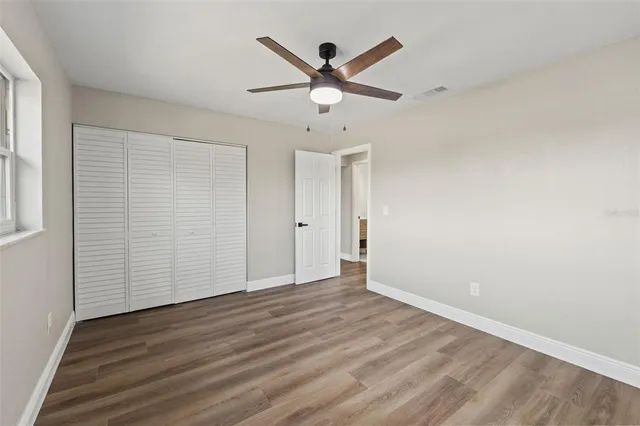 an empty room with wooden floor ceiling fan and windows