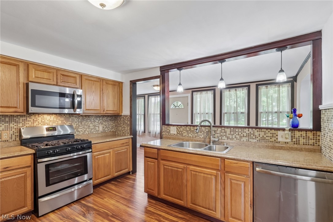 4188 Manchester Road Perry, OH 44081 - Photo 19 of 41 Kitchen featuring wood-finish flooring, oak cabinetry, stainless steel appliances, mosaic tile backsplash, and a double basin stainless steel sink