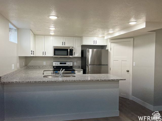 702 North 100 West Logan, UT 84321 - Photo 53 of 58 Kitchen featuring a textured ceiling, white cabinets, a peninsula, light stone countertops, and appliances with stainless steel finishes