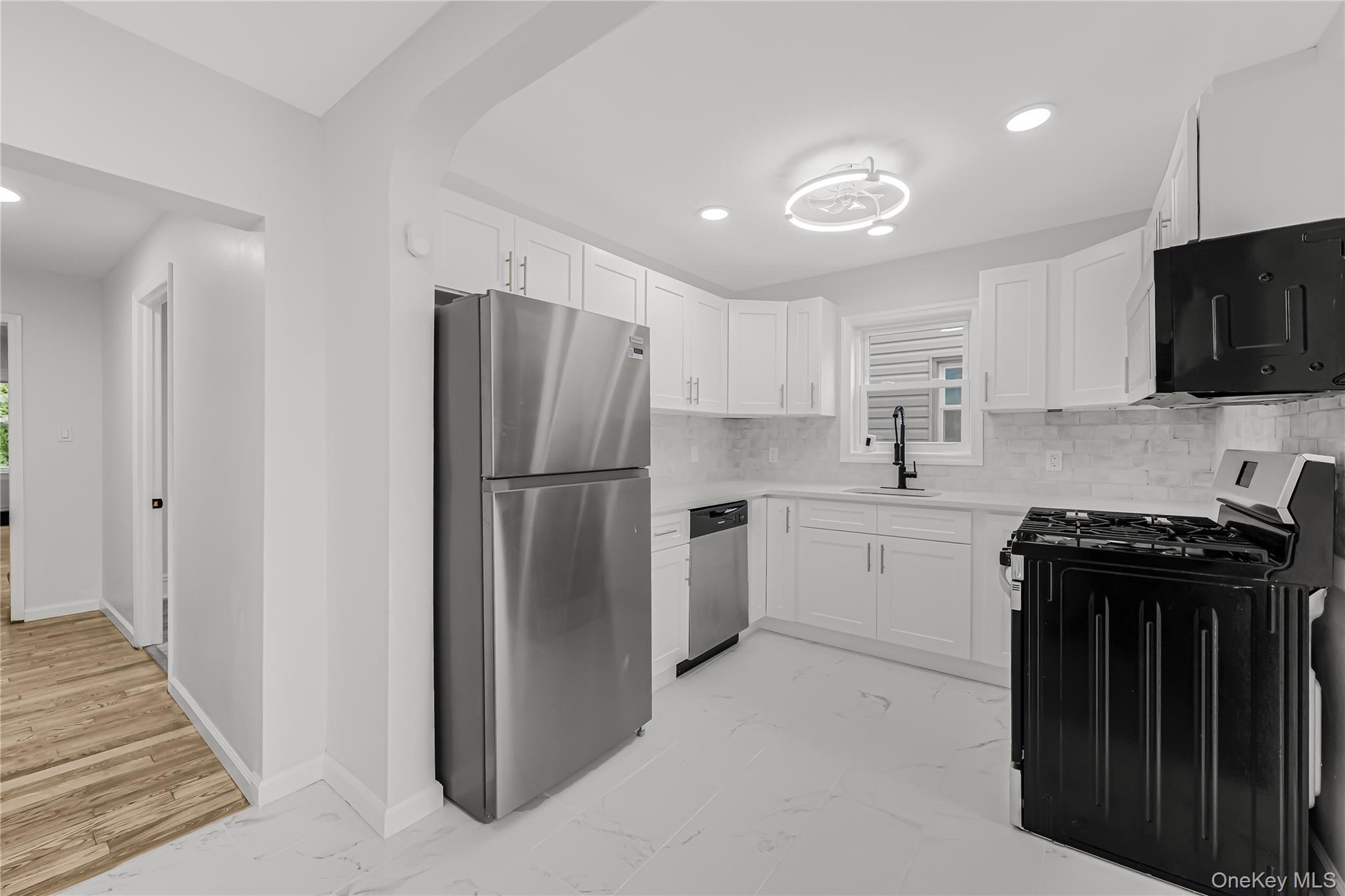 173-43 103rd Road Queens, NY 11433 - Photo 5 of 43 Kitchen featuring white shaker cabinetry, stainless steel appliances, a tile backsplash, and a modern ceiling light fixture