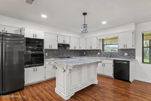 a kitchen with stainless steel appliances granite countertop a stove a sink dishwasher a refrigerator white cabinets and wooden floor