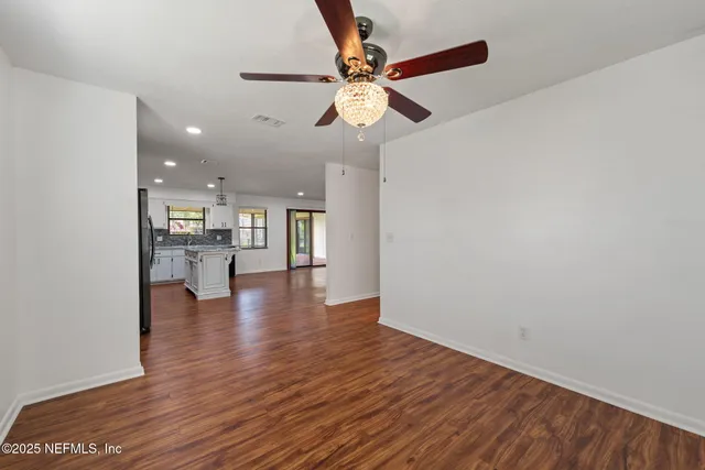 a view of an empty room with wooden floor and a ceiling fan