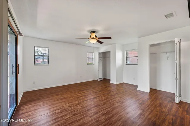 an empty room with wooden floor chandelier fan and windows