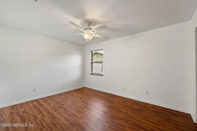an empty room with wooden floor fan and windows