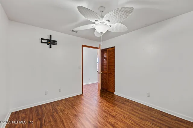 an empty room with wooden floor fan and windows