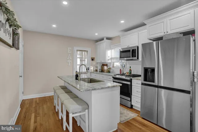 a kitchen with stainless steel appliances granite countertop a refrigerator a stove and a sink with wooden floor