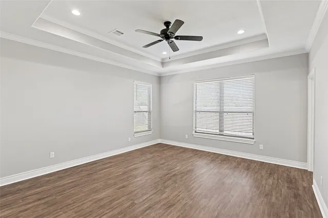 an empty room with wooden floor ceiling fan and windows