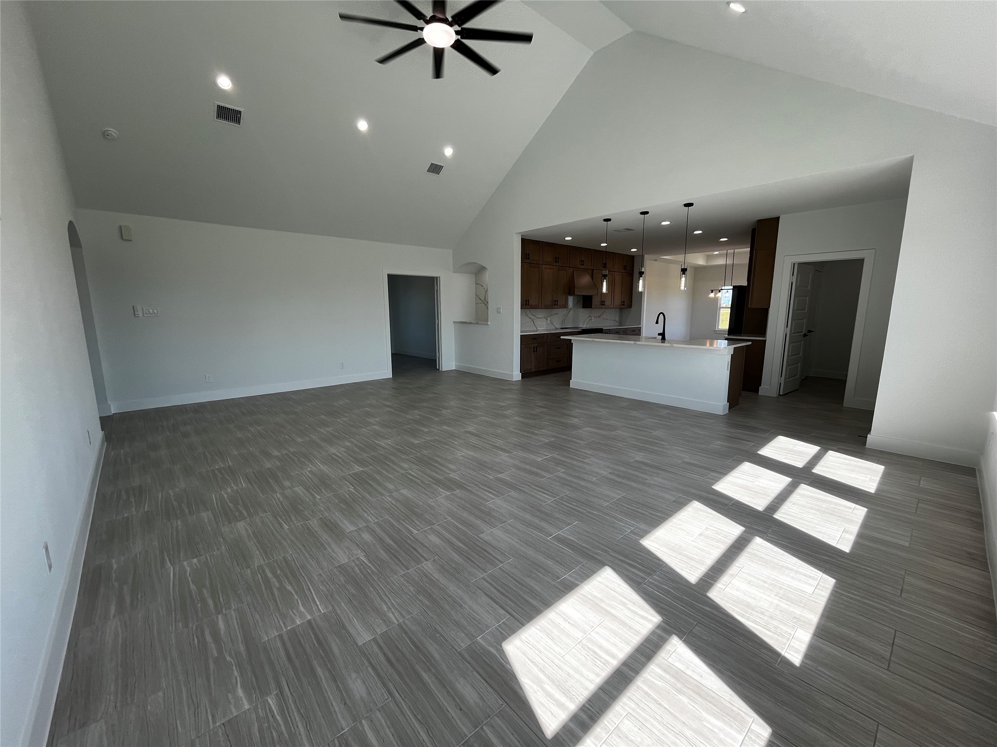 471 Buffalo Trail Angleton, TX 77515 - Photo 4 of 35 This spacious, open-concept living area features high ceilings, modern tile flooring, and ample natural light. The kitchen boasts a stylish island with pendant lighting, wood cabinets, and a sleek faucet. Ideal for entertaining.