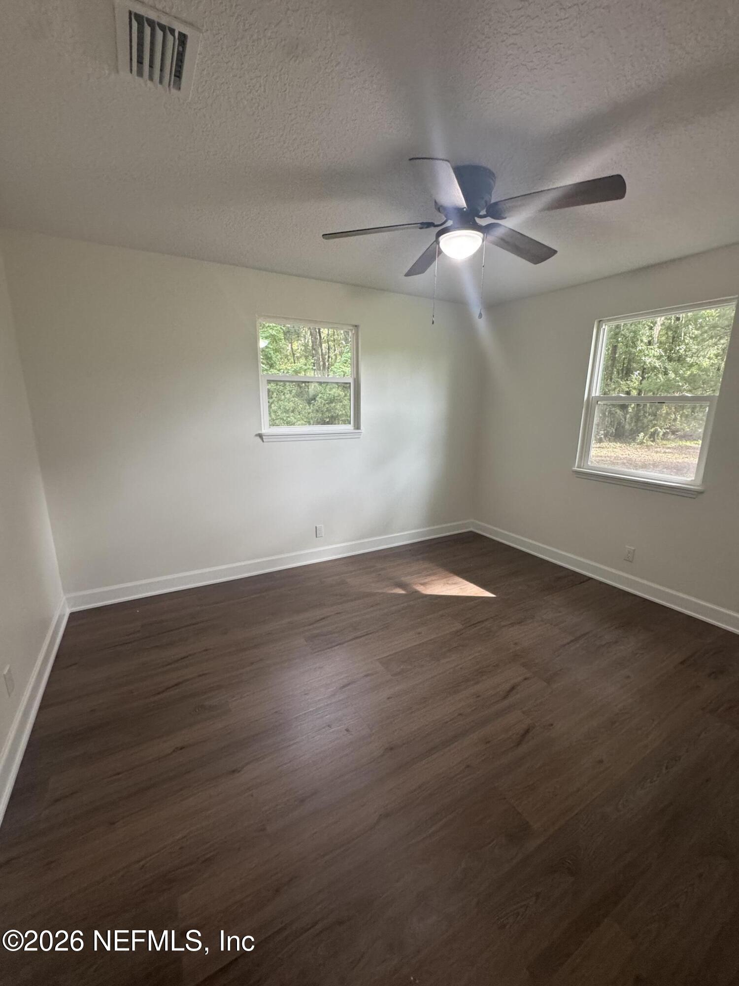 5202 Southwest 155th Street Starke, FL 32091 - Photo 11 of 13 an empty room with wooden floor chandelier fan and windows
