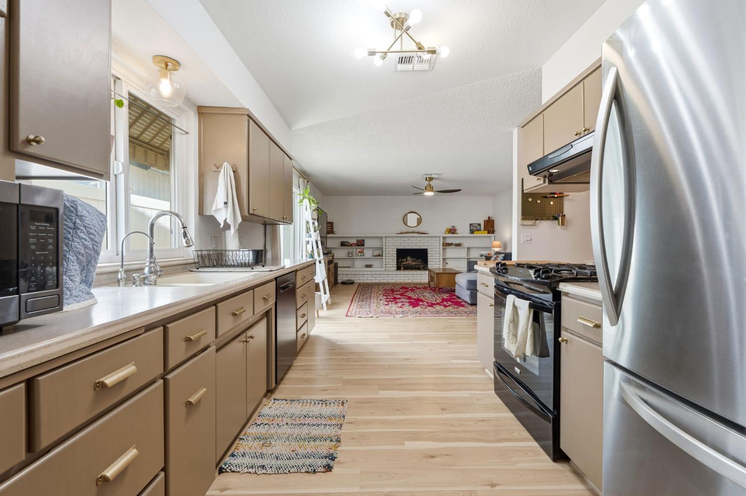 905 Redwood Lane Lemoore, CA 93245 - Photo 27 of 56 a large kitchen with stainless steel appliances granite countertop a refrigerator oven a sink dishwasher and a fireplace with wooden floor