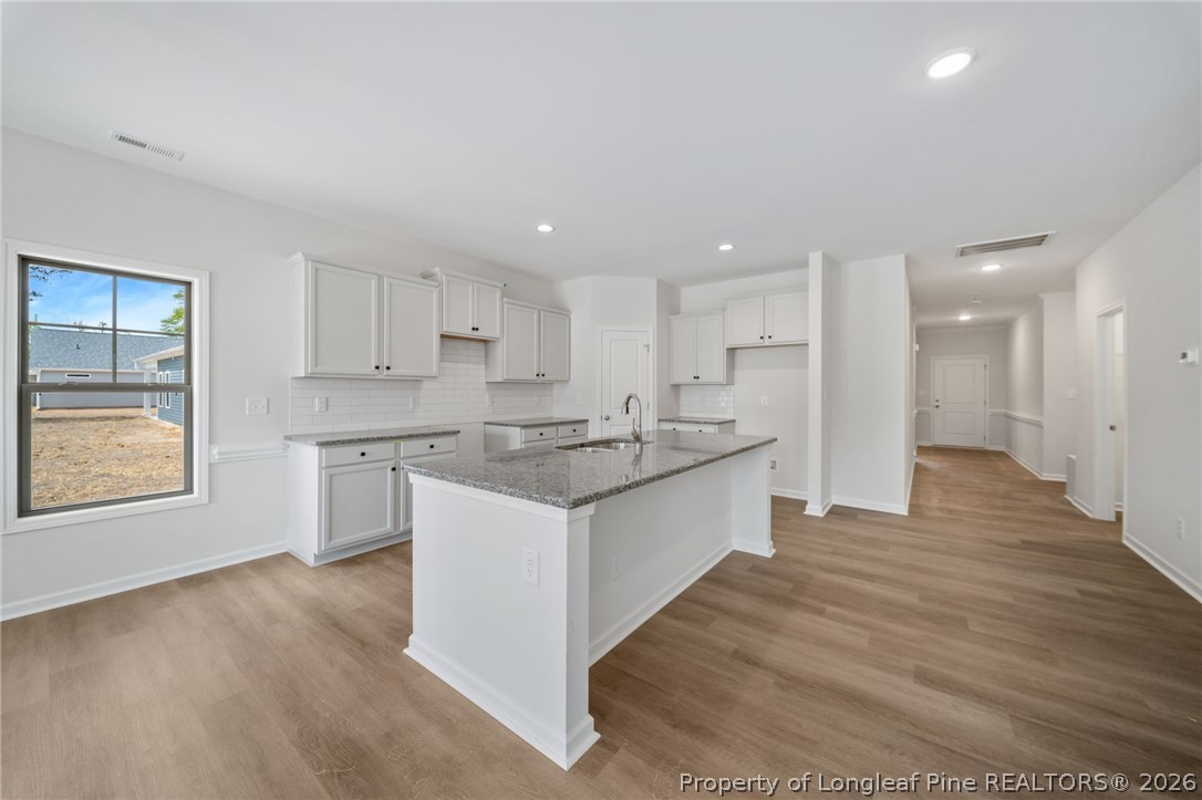 4038 Lofton Street Wade, NC 28395 - Photo 12 of 29 a large kitchen with stainless steel appliances granite countertop a stove a sink a refrigerator and white cabinets with wooden floor