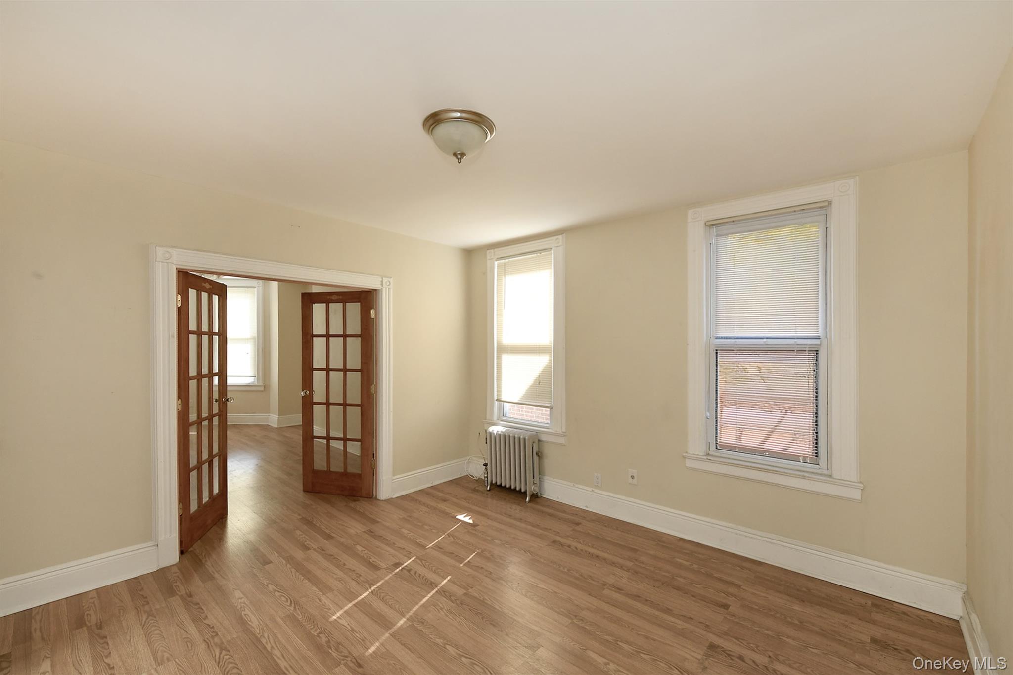 30-94 47th Street Queens, NY 11103 - Photo 7 of 20 Empty room with french doors, wood finished floors, and radiator