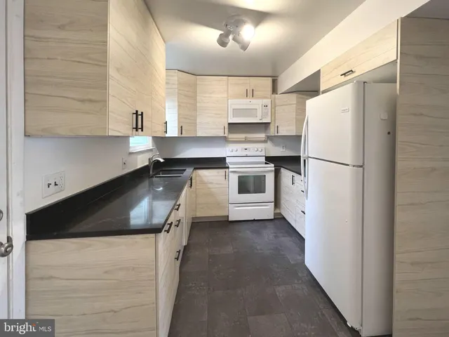 a kitchen with granite countertop a refrigerator a sink a stove and white cabinets