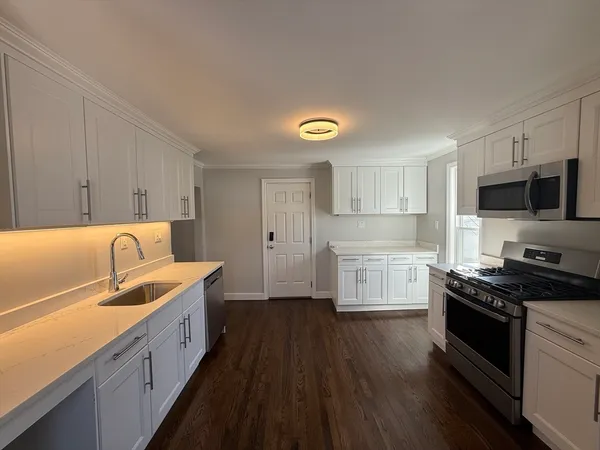 a kitchen with granite countertop a sink dishwasher stove and white cabinets with wooden floor