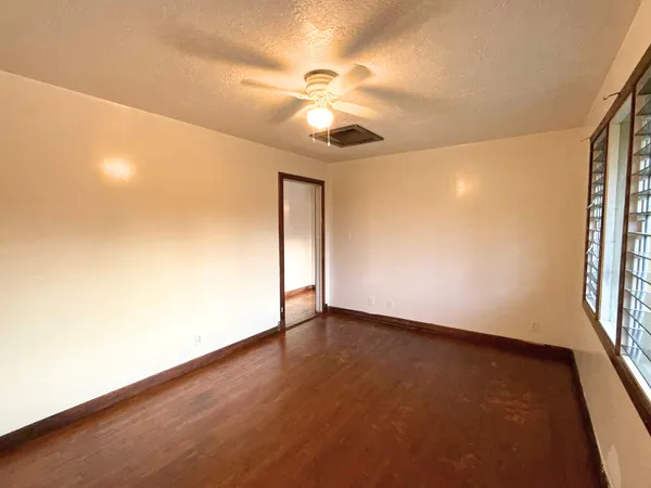 an empty room with wooden floor fan and windows