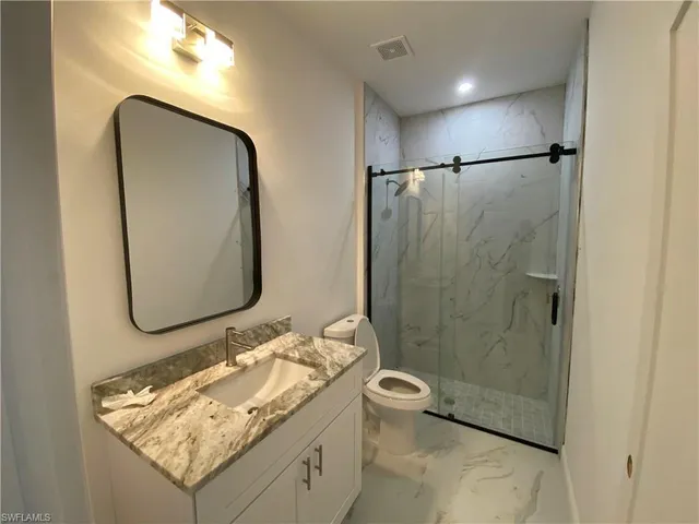 a bathroom with a granite countertop sink a toilet and shower