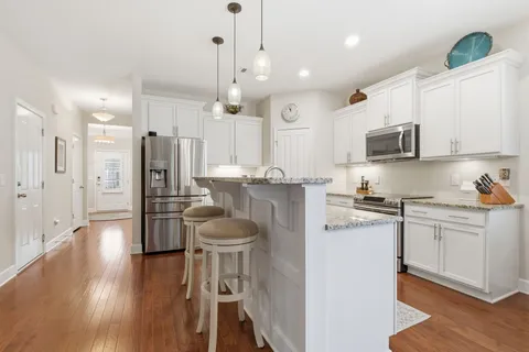 a kitchen with stainless steel appliances granite countertop a refrigerator a stove a sink dishwasher and white cabinets with wooden floor