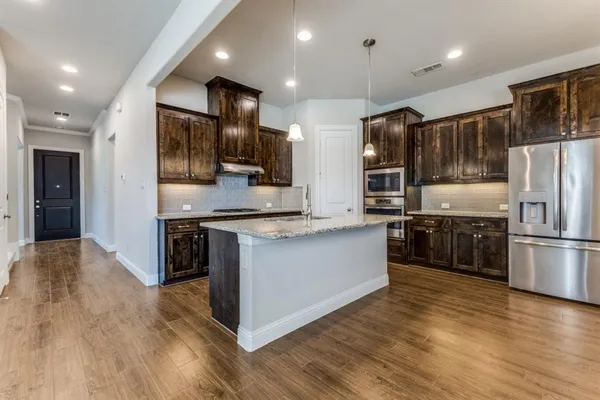 a kitchen with stainless steel appliances kitchen island granite countertop a refrigerator a sink a stove a microwave and wooden floor