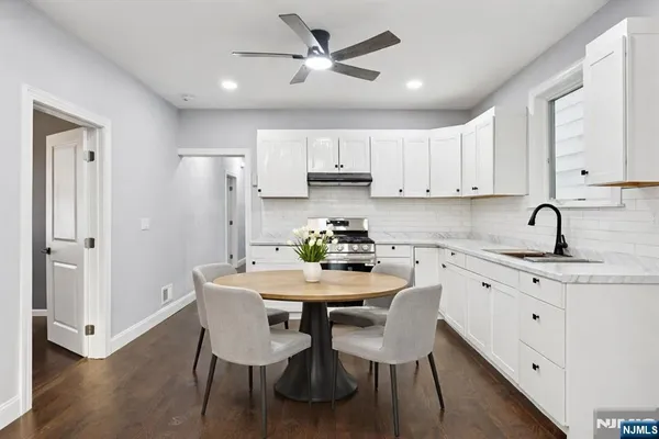 a kitchen with stainless steel appliances granite countertop a dining table chairs a refrigerator a sink a stove a microwave with white cabinets and wooden floor