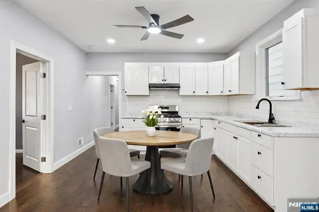 a kitchen with stainless steel appliances granite countertop a dining table chairs a refrigerator a sink a stove a microwave with white cabinets and wooden floor