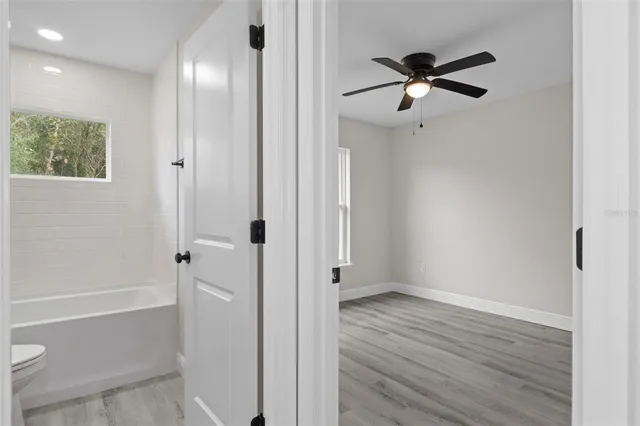 an empty room with wooden floor ceiling fan and windows