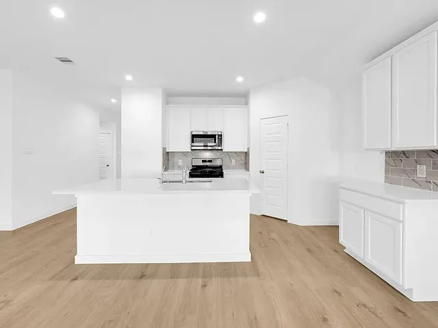 a large white kitchen with kitchen island a sink a stove a refrigerator and white cabinets