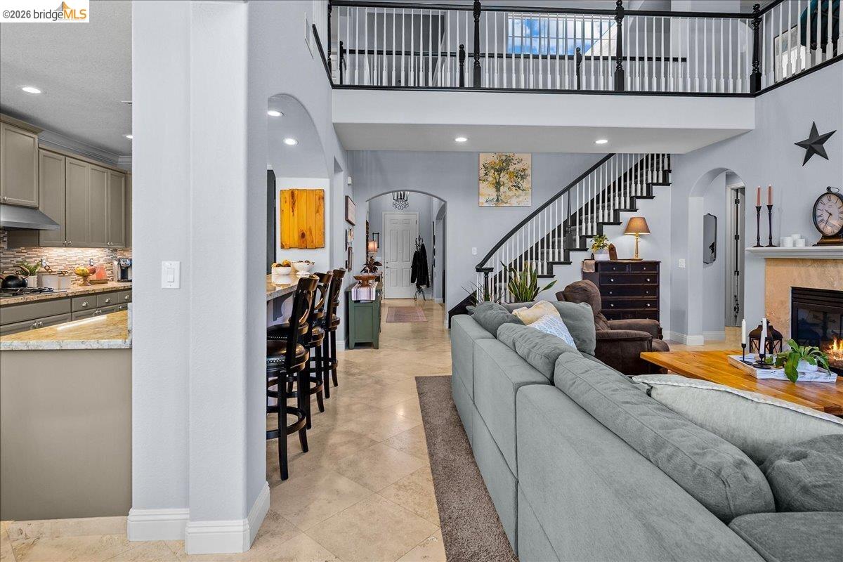 653 Bouma Lane Ripon, CA 95366 - Photo 17 of 39 Vaulted ceilings with a second-story overlook, grand staircase with dark wood-finish handrails, kitchen featuring light-colored cabinetry and stone-finish countertops, fireplace with a stone-finish surround, and tile flooring throughout
