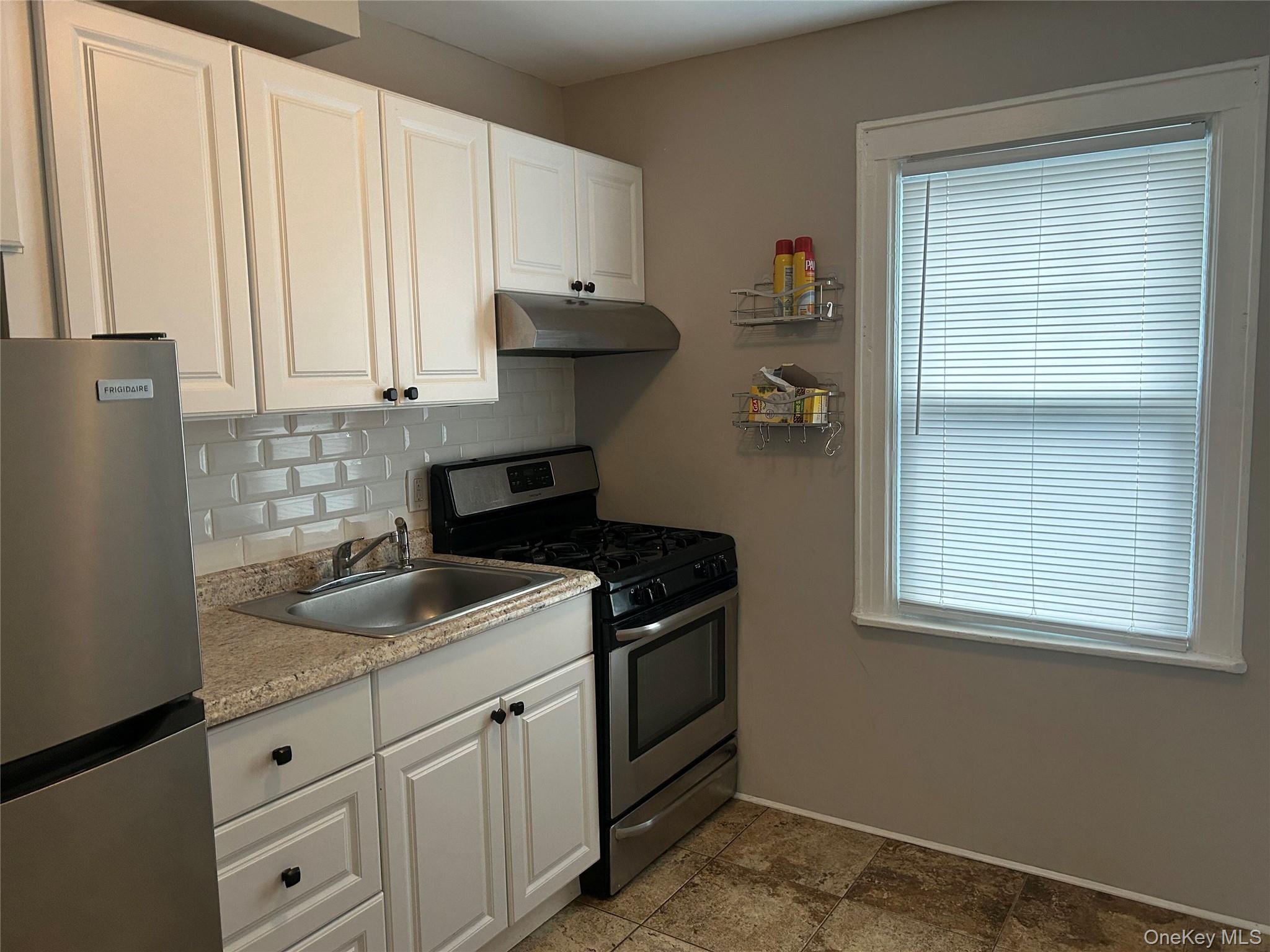 248-15 89th Avenue, Unit 2 Queens, NY 11426 - Photo 3 of 9 Kitchen with appliances with stainless steel finishes, white cabinetry, light countertops, under cabinet range hood and backsplash
