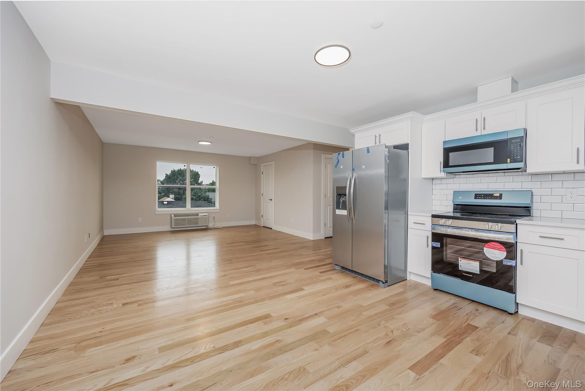 539 Front Street, Unit 4C Hempstead, NY 11550 - Photo 2 of 17 Kitchen featuring appliances with stainless steel finishes, white cabinetry, decorative backsplash, and light wood finished floors