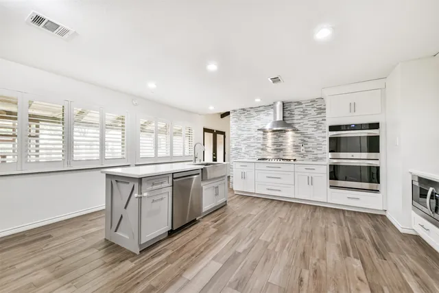 a large kitchen with stainless steel appliances a large counter top a stove and a wooden floors