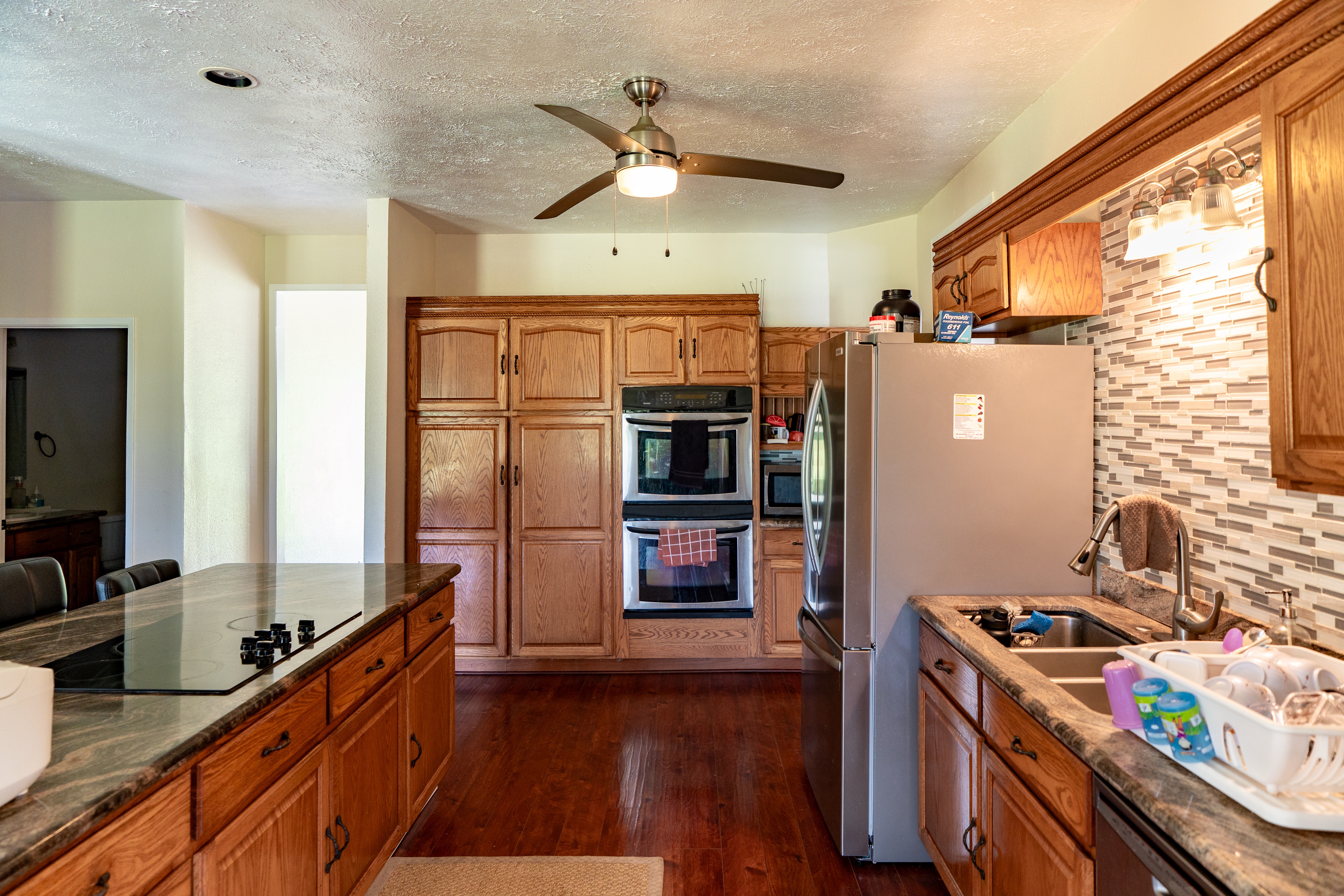 17-4044 South Road Keaau, HI 96749 - Photo 6 of 28 a kitchen with stainless steel appliances a stove top oven a refrigerator a sink and dishwasher with wooden floor